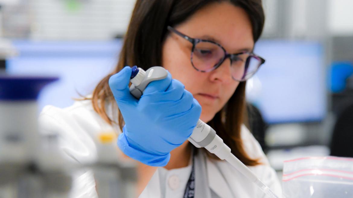 mujer joven con guantes azules en laboratorio pipeteando